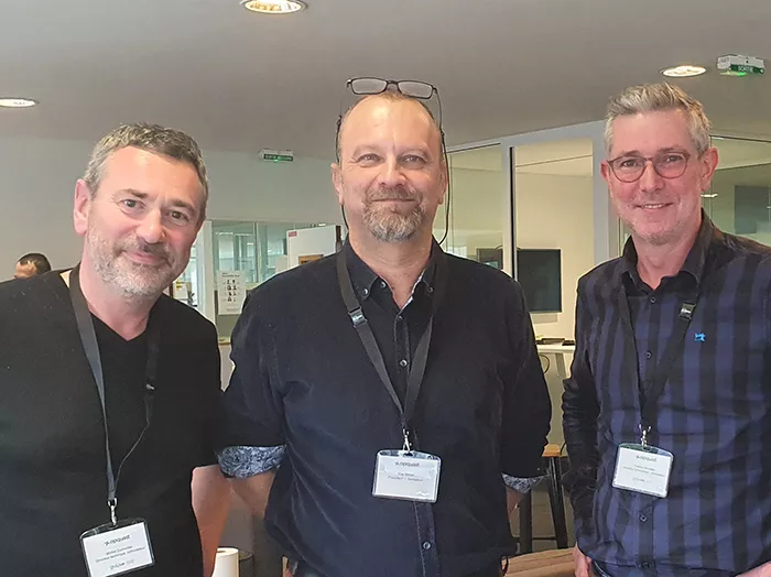 Trois hommes côte à côte, badge au cou, lors d’une rencontre.